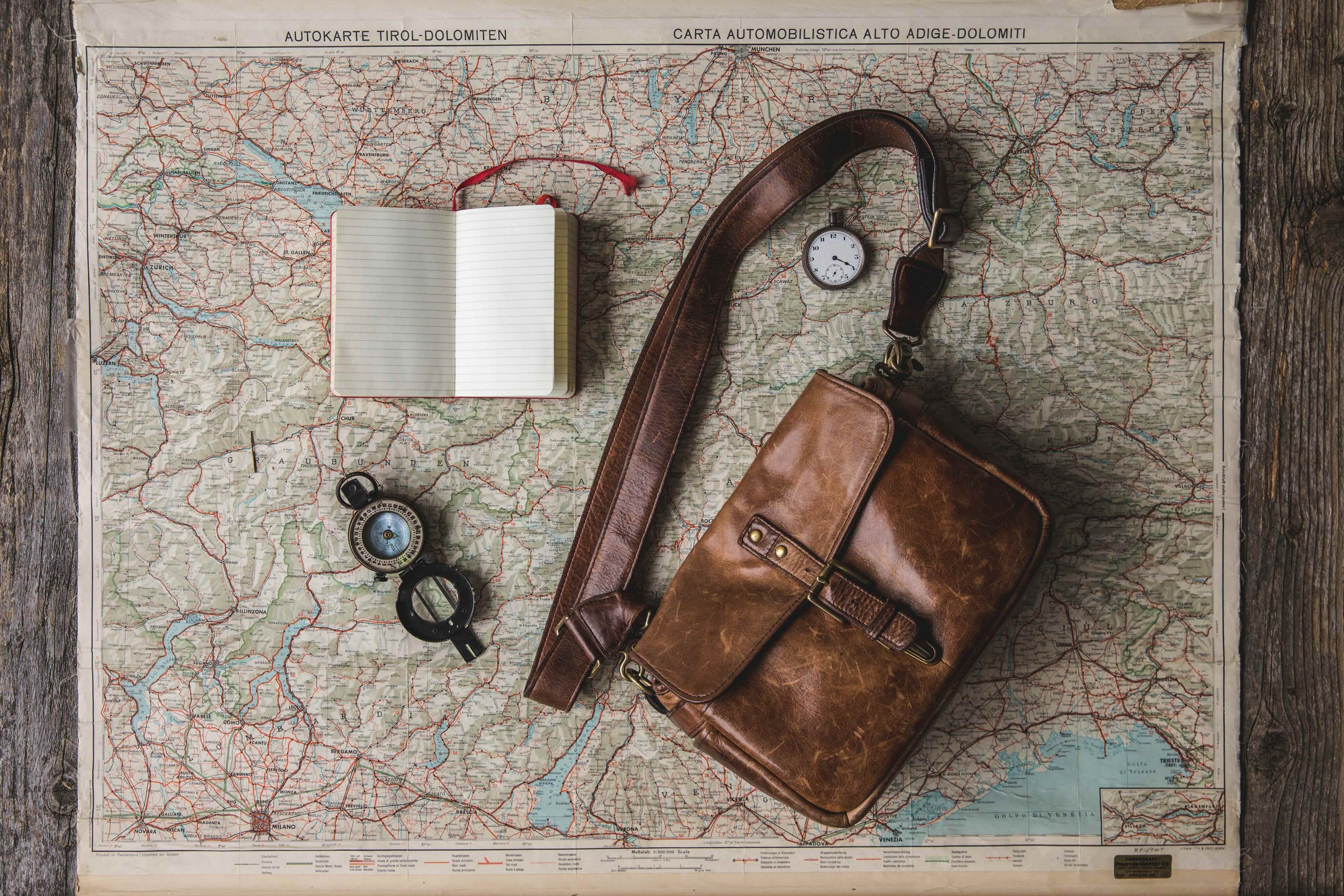 travel bag, compass, pocket watch and notebook - all lying on a map